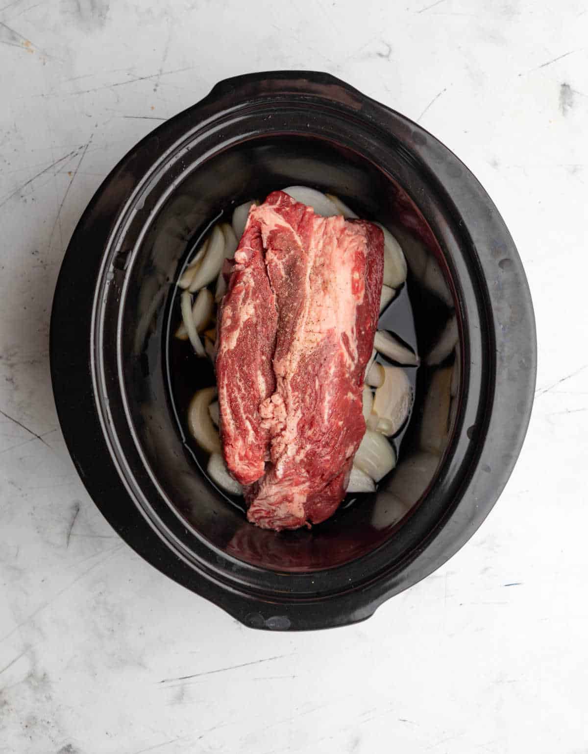 Beef broth poured around a chuck roast in a crock pot. 