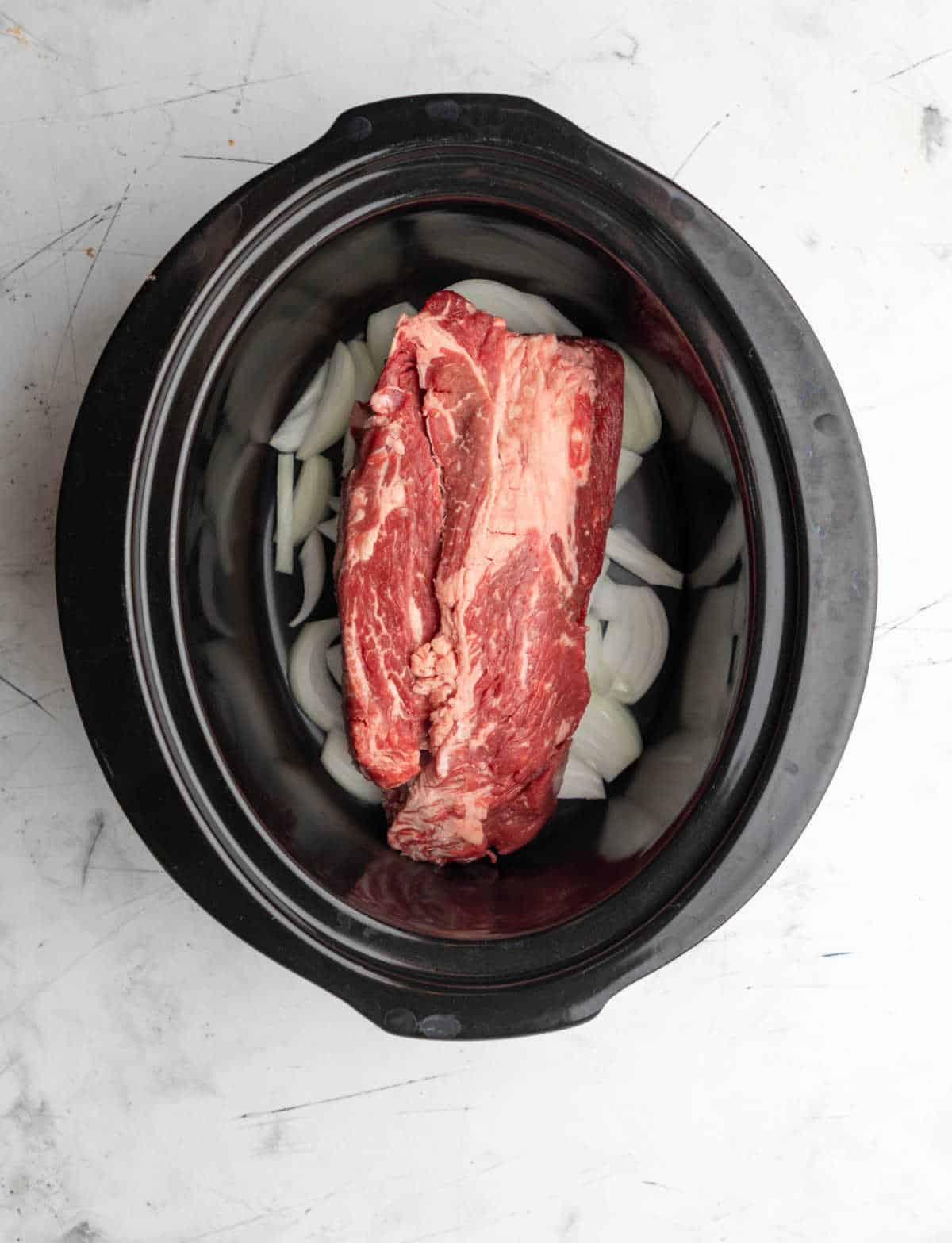 A chuck roast over sliced onions in a crock pot. 