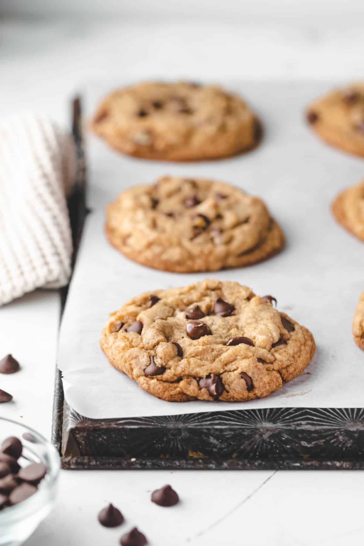 Three huge chocolate chip cookies on a piece of parchment paper. 