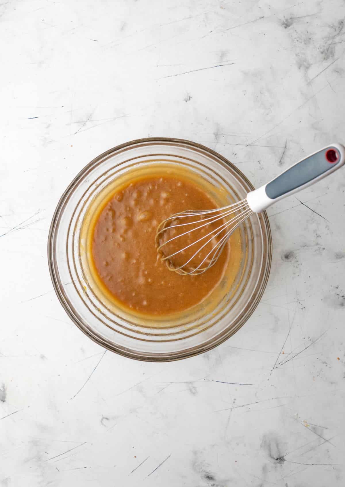 Butter and sugars stirred together in a glass mixing bowl. 