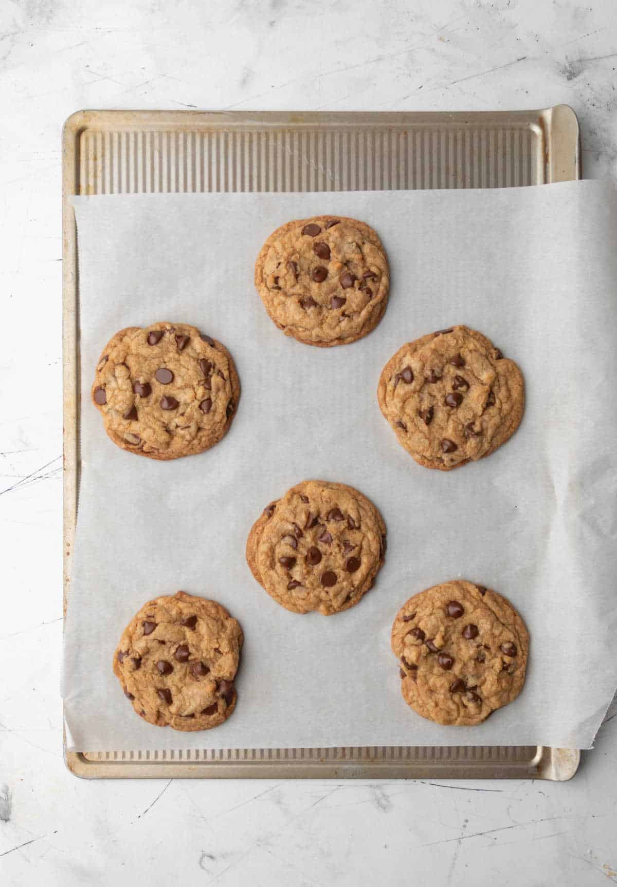 Six baked thick chocolate chip cookies on a baking sheet. 