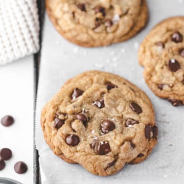 Two thick chocolate chip cookies in a row on a piece of parchment paper.