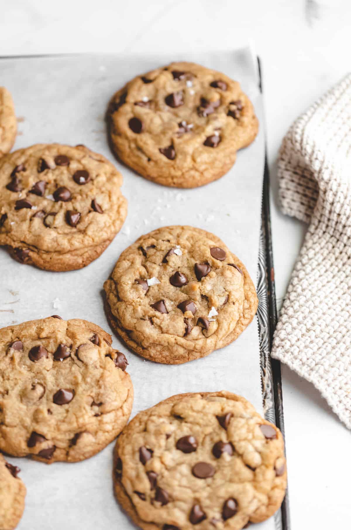 Rows of thick chocolate chip cookies next to a tan cloth. 