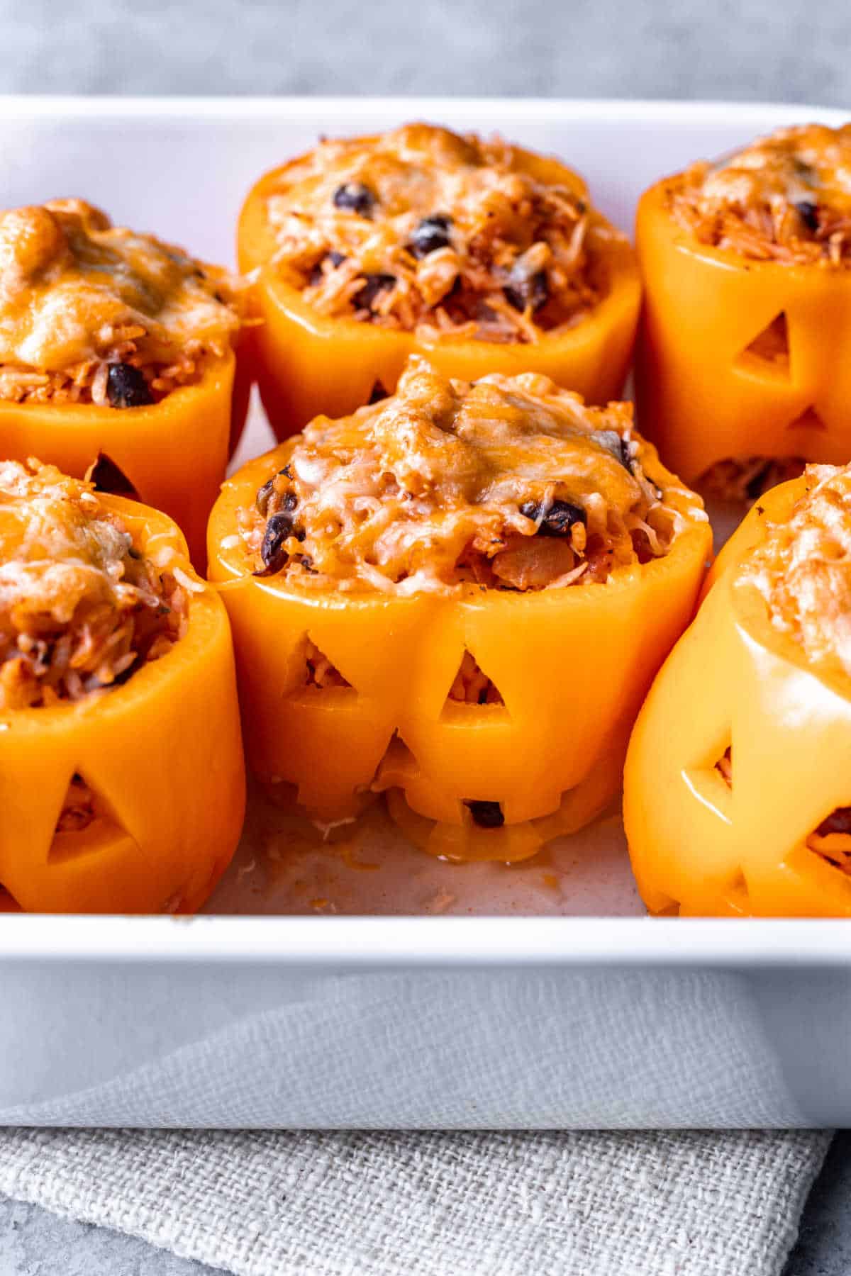 Baked jack-o'-lantern stuffed peppers in a baking dish.