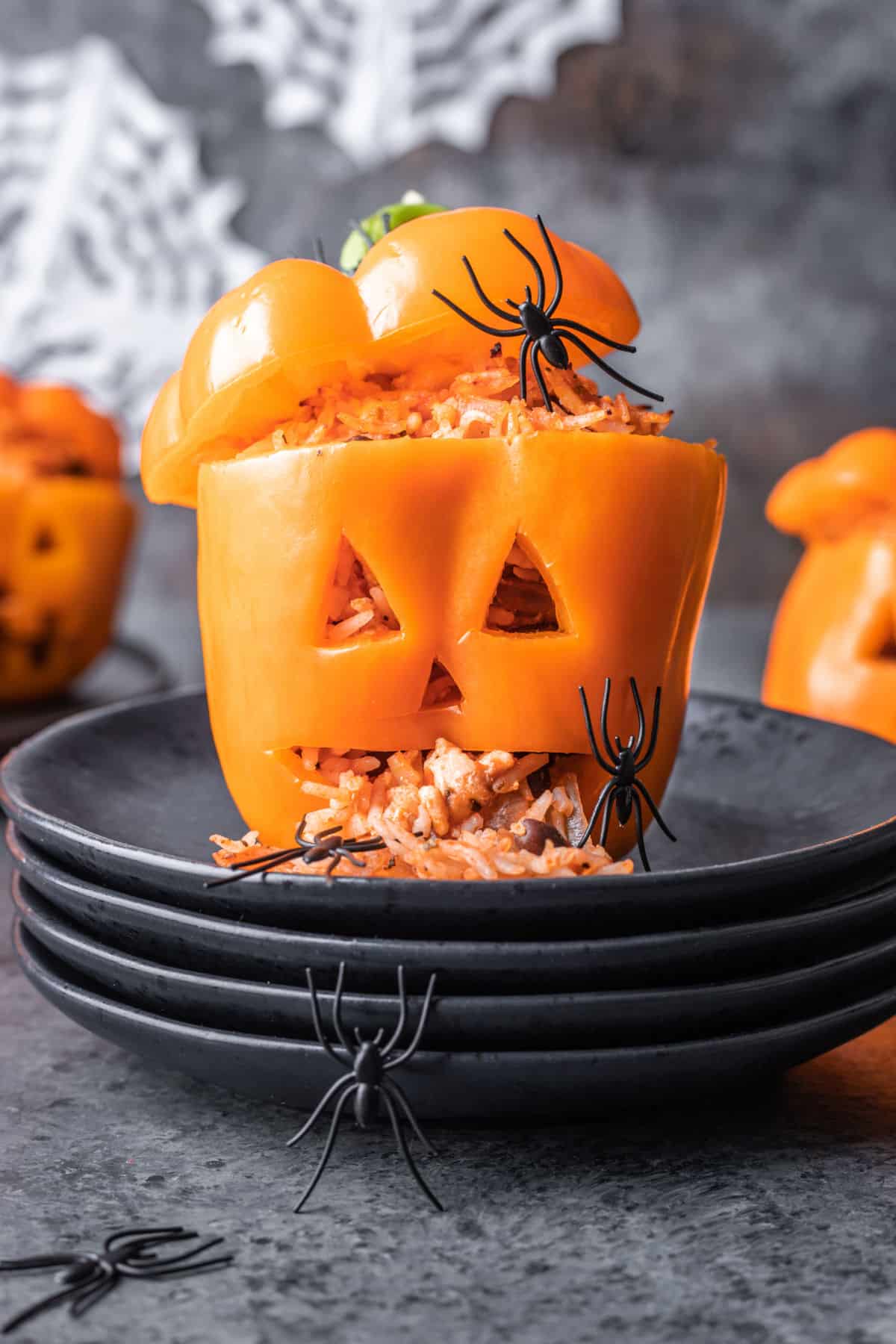Jack-o'-lantern stuffed pepper on stack of three black plates.