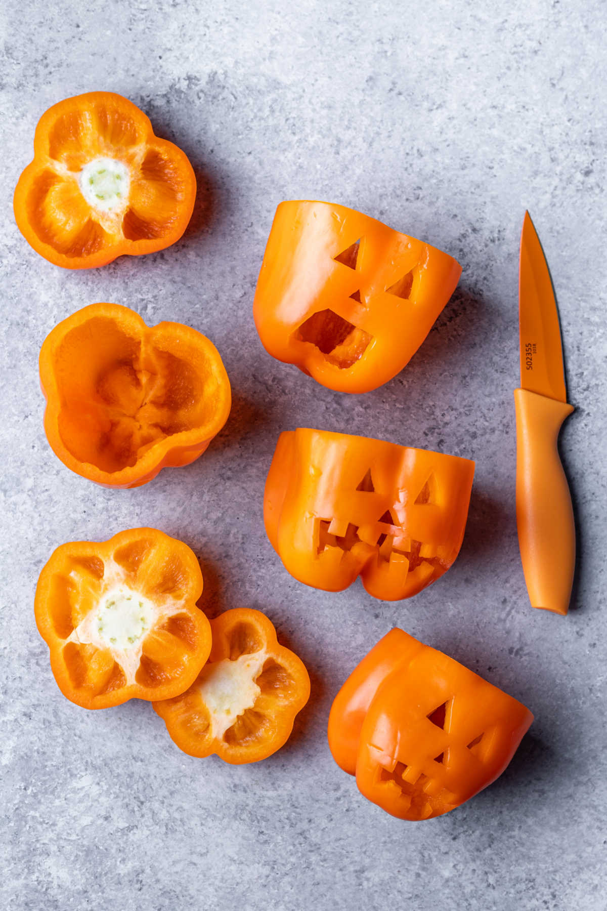 A paring knife next to three orange bell peppers with faces cut in them. 