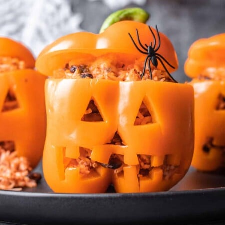 Three jack-o'-lantern stuffed peppers on a gray plate.