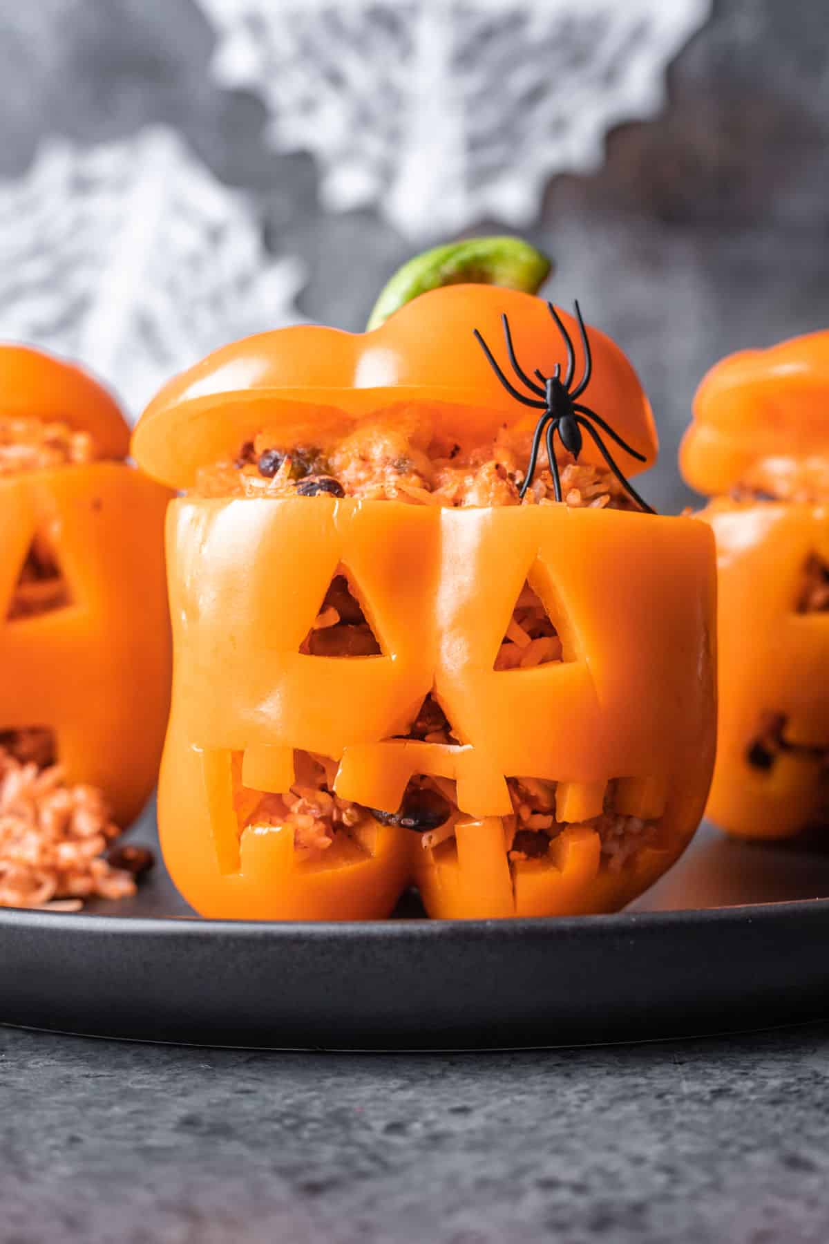 Three jack-o'-lantern stuffed peppers on a gray plate. 