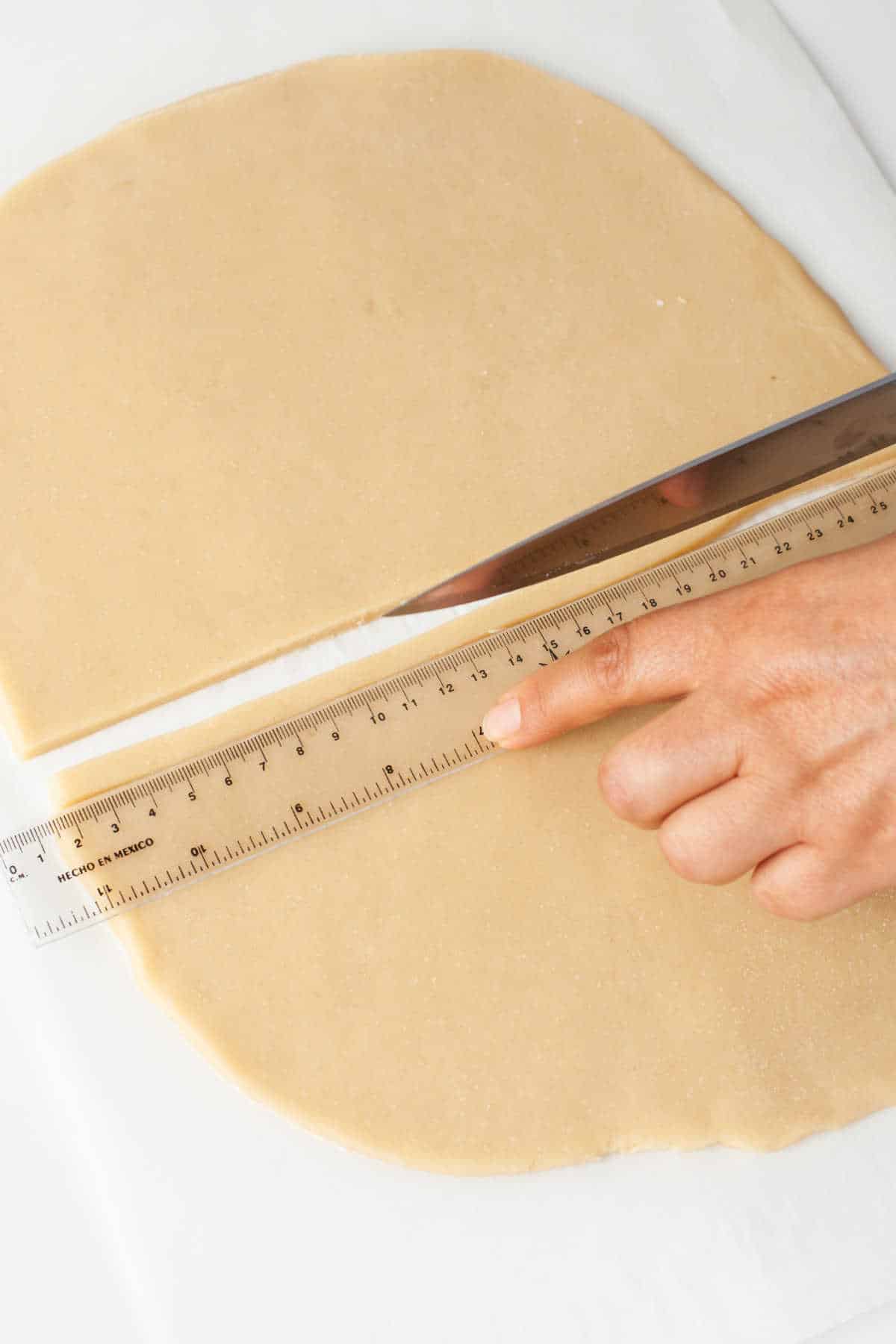 A knife cutting a strip of pie dough along a ruler. 
