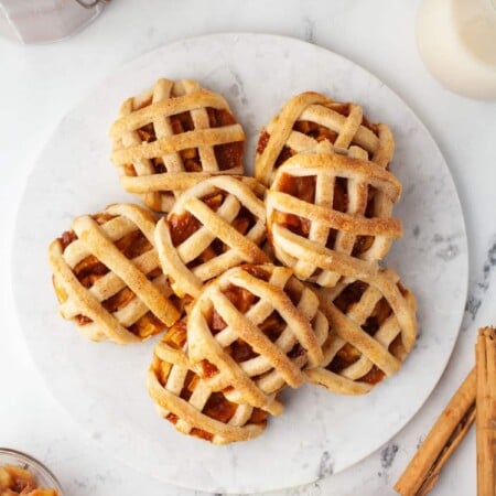 Stack of apple pie cookies surrounded by cinnamon sticks apples and flour cannister.