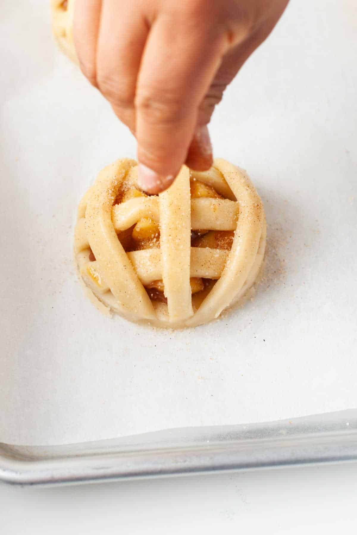 A hand sprinkling cinnamon sugar onto an unbaked apple pie cookie. 