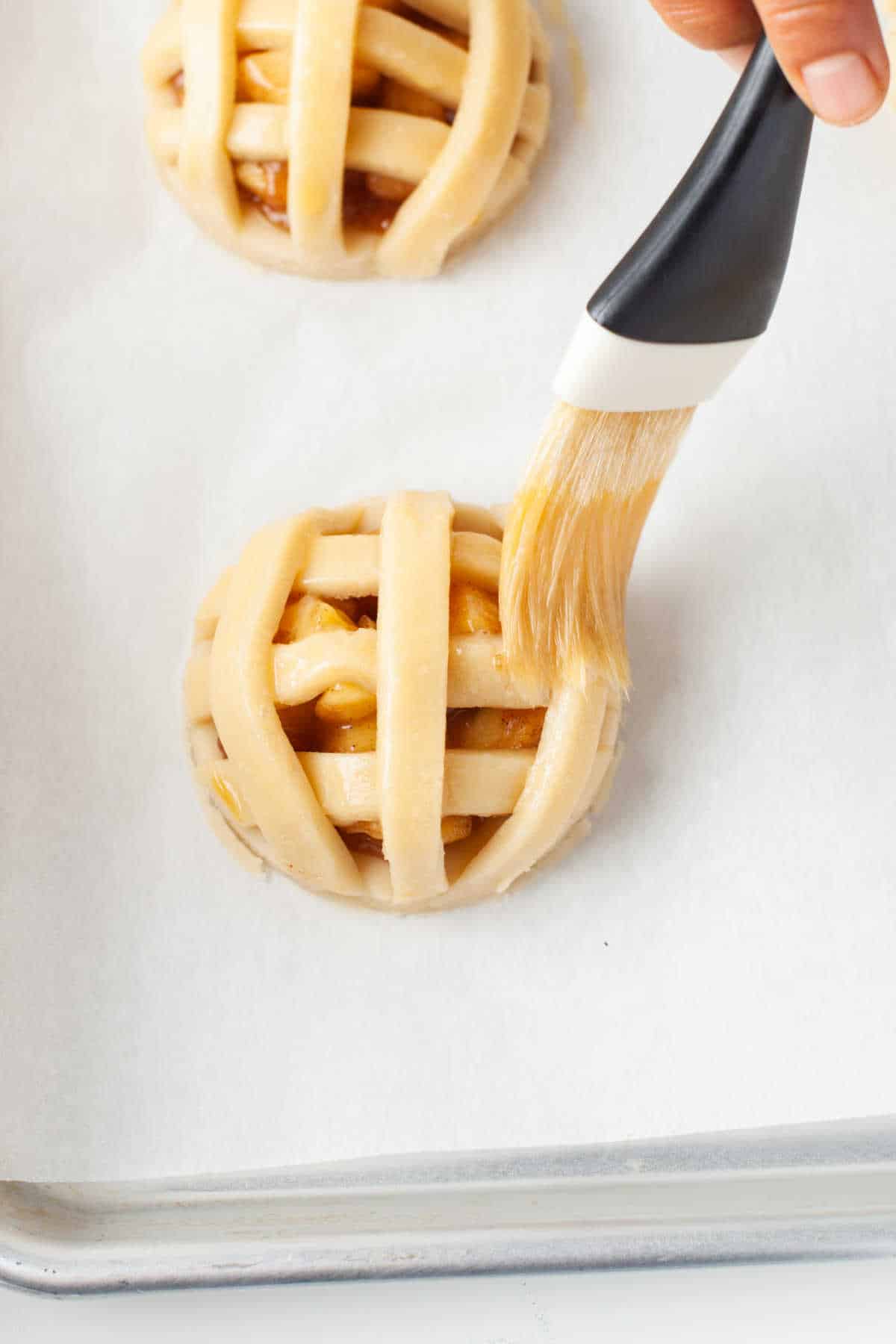 A pastry brush brushing egg wash onto apple pie cookies. 