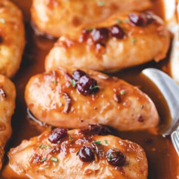 Baked cranberry chicken in a white baking dish with a spoon in it.