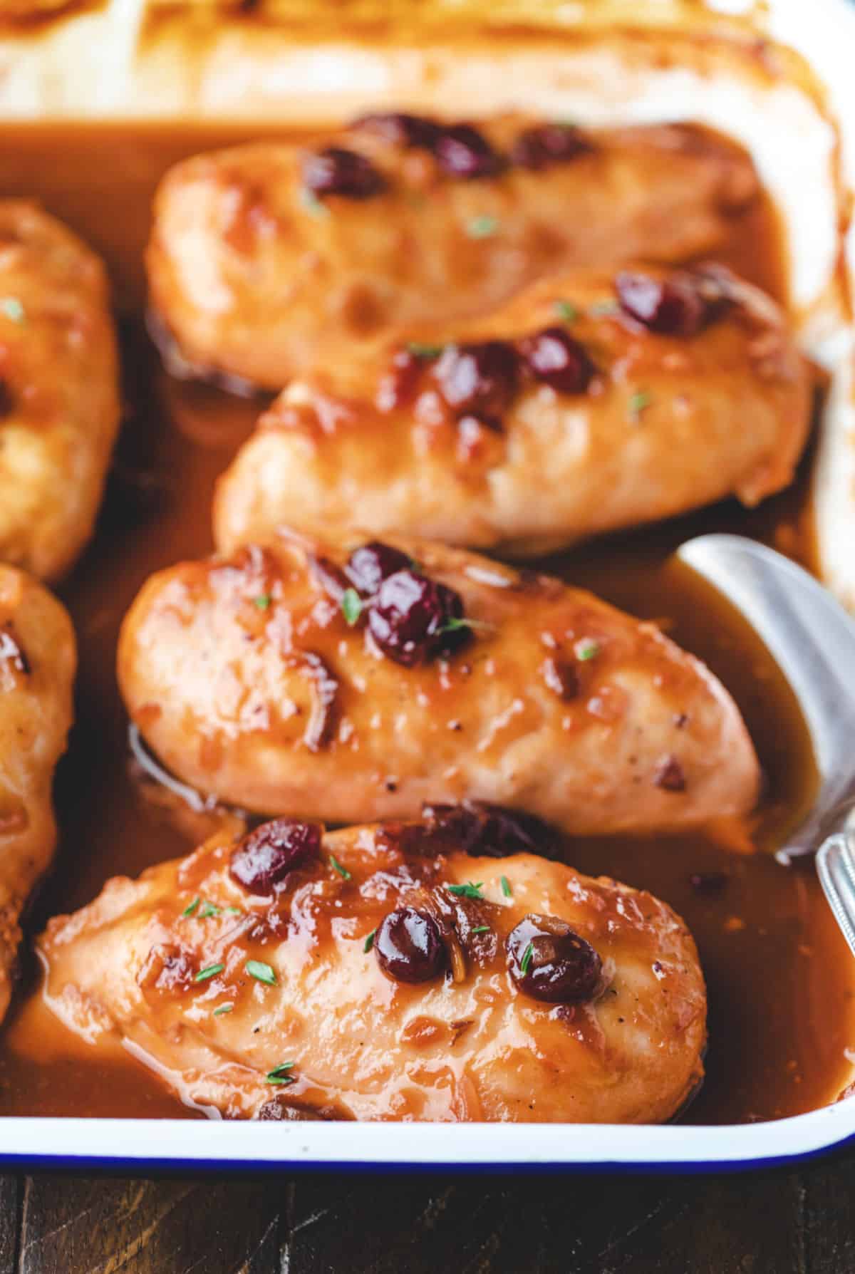 Baked cranberry chicken in a white baking dish with a spoon in it. 