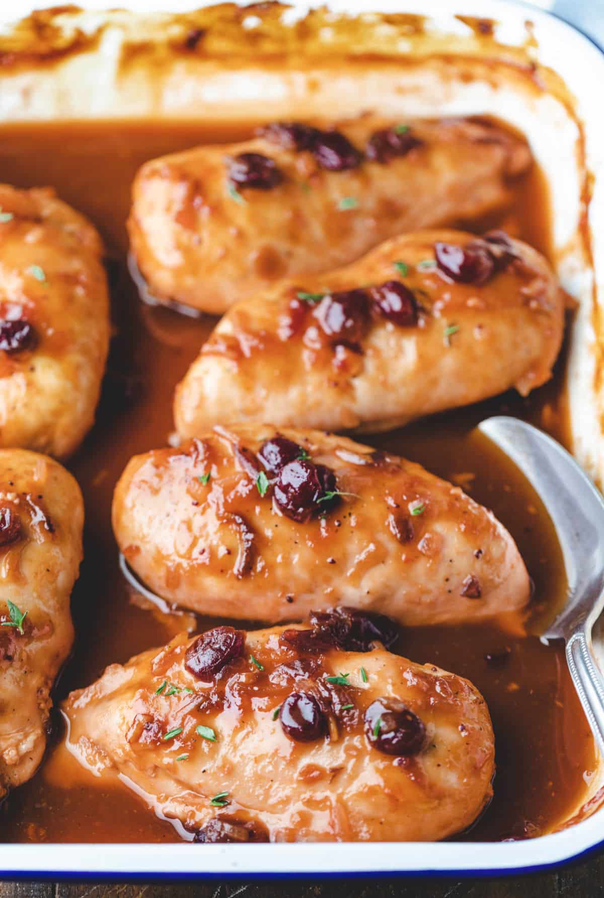 White pan full of baked cranberry chicken and sauce. 