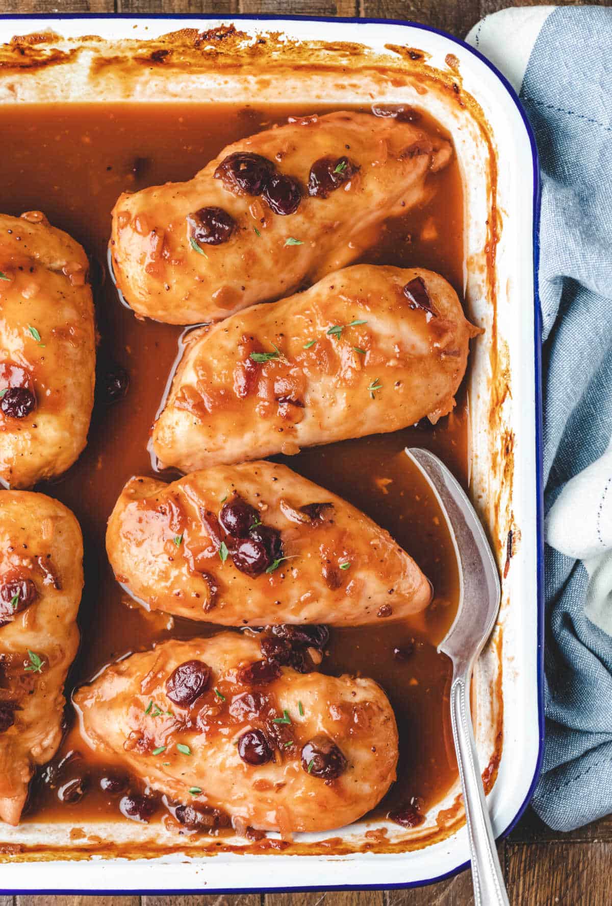 Pan of cranberry chicken next to a blue dish towel. 