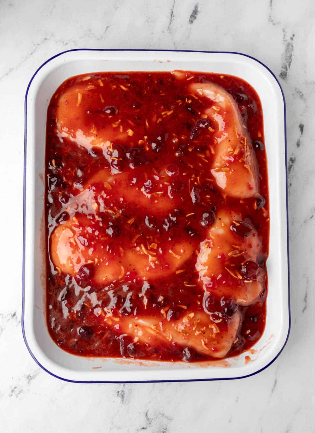 Cranberry sauce over chicken in a white baking pan. 
