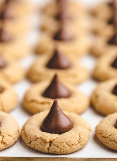 A row of peanut blossom cookies on a parchment lined cookie sheet.