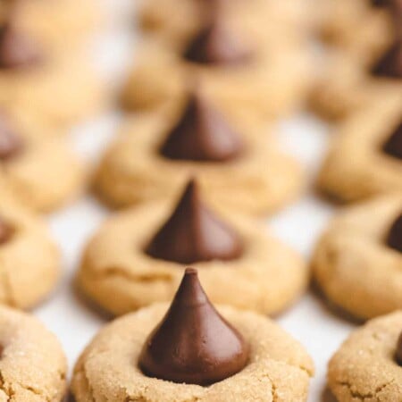 A row of peanut blossom cookies on a parchment lined cookie sheet.