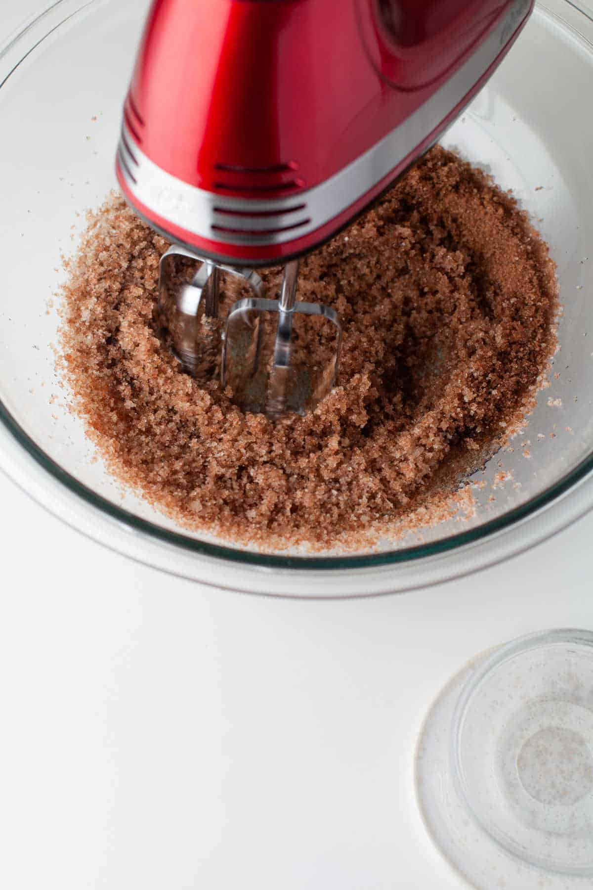 Hand mixer beating oil and sugars together in a glass mixing bowl. 