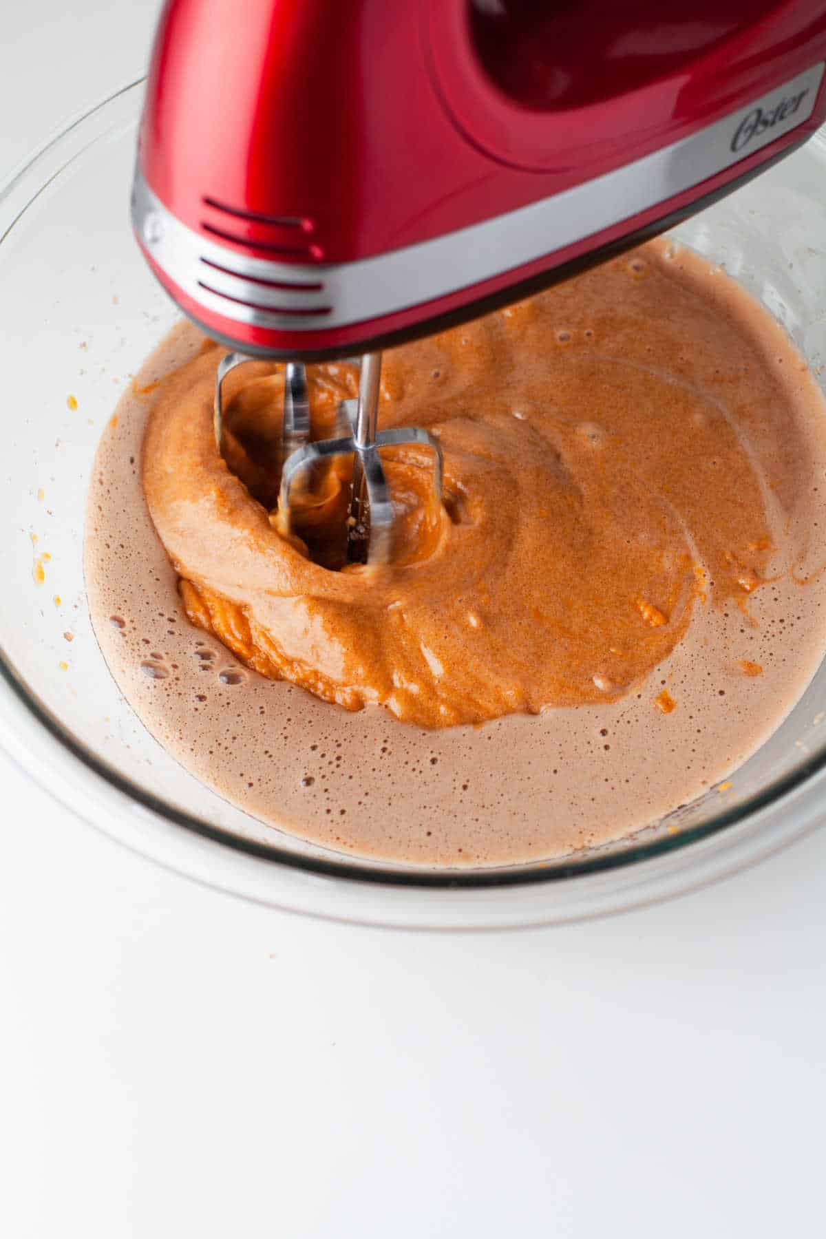 Hand mixer beating pumpkin puree into oil and sugar mixture. 