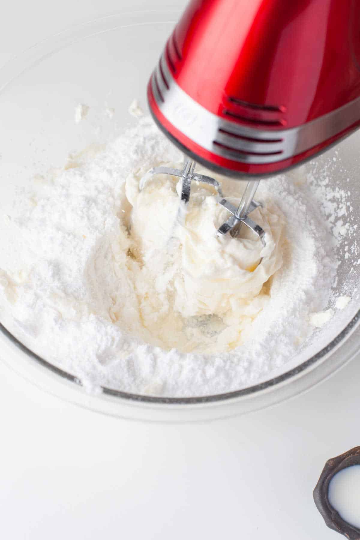 Hand mixer beating powdered sugar into cream cheese and butter. 
