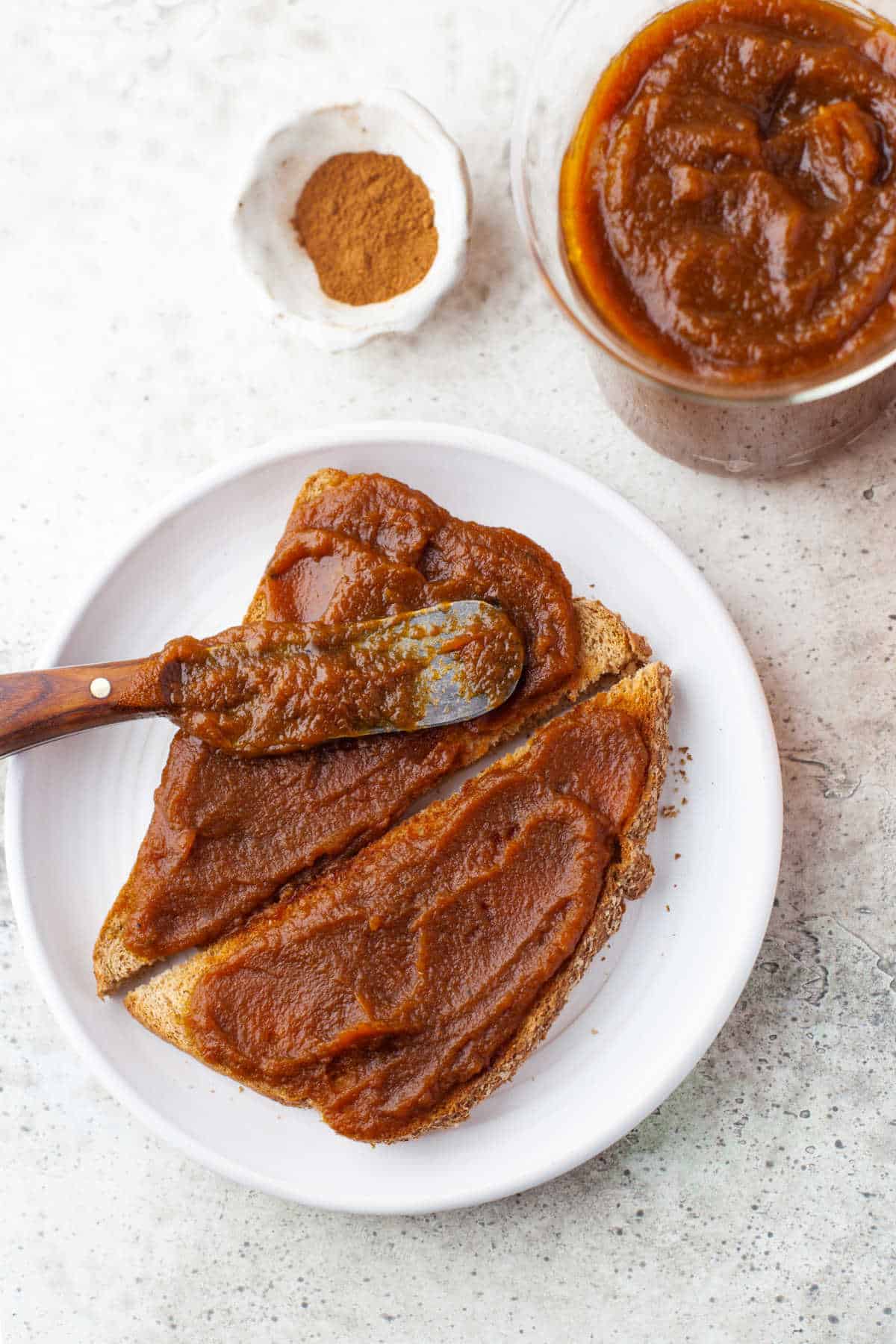 A wooden knife spreading pumpkin butter on toast. 