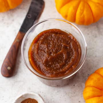 A glass jar full of pumpkin butter next to three mini pumpkins.