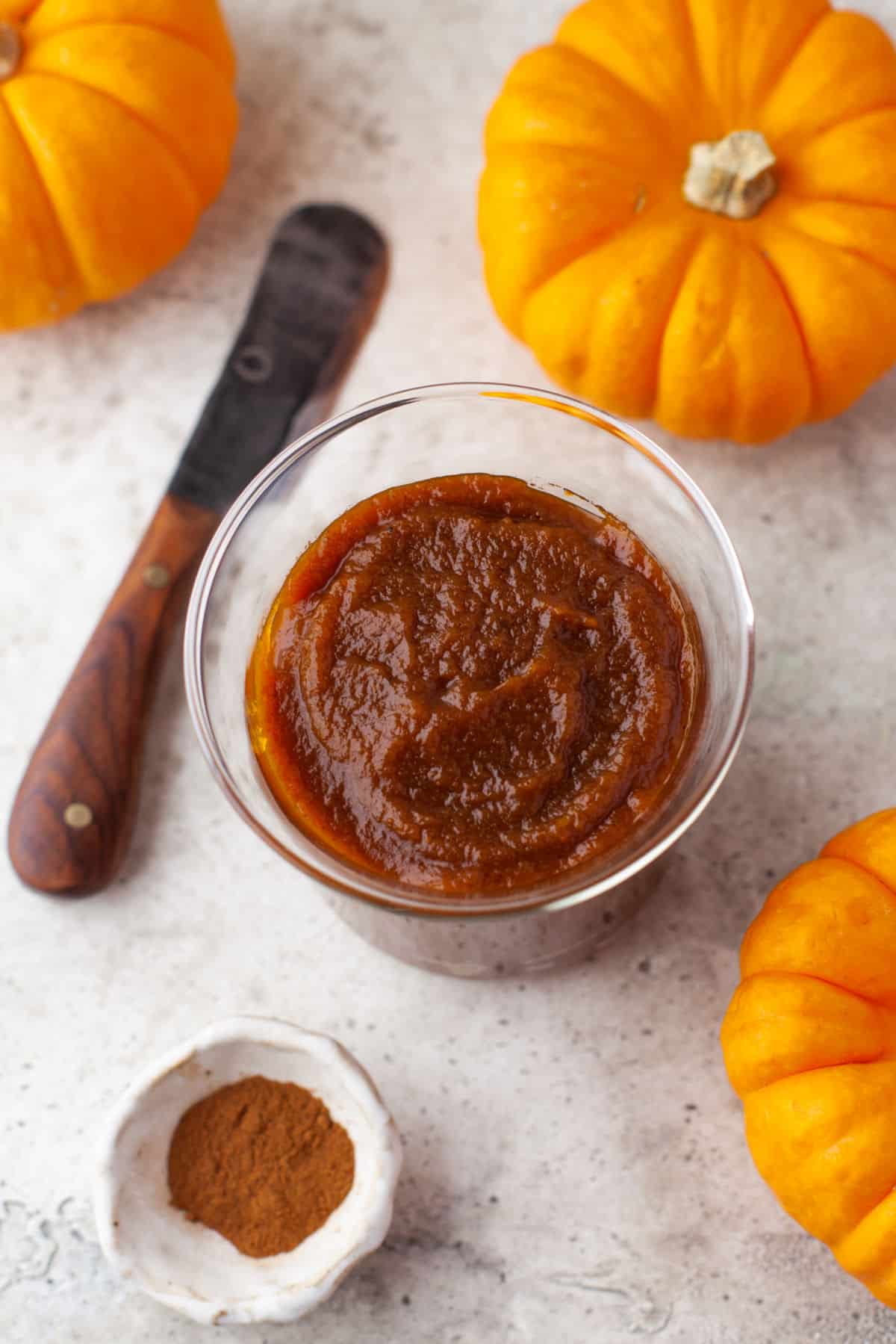 A glass jar full of pumpkin butter next to three mini pumpkins.