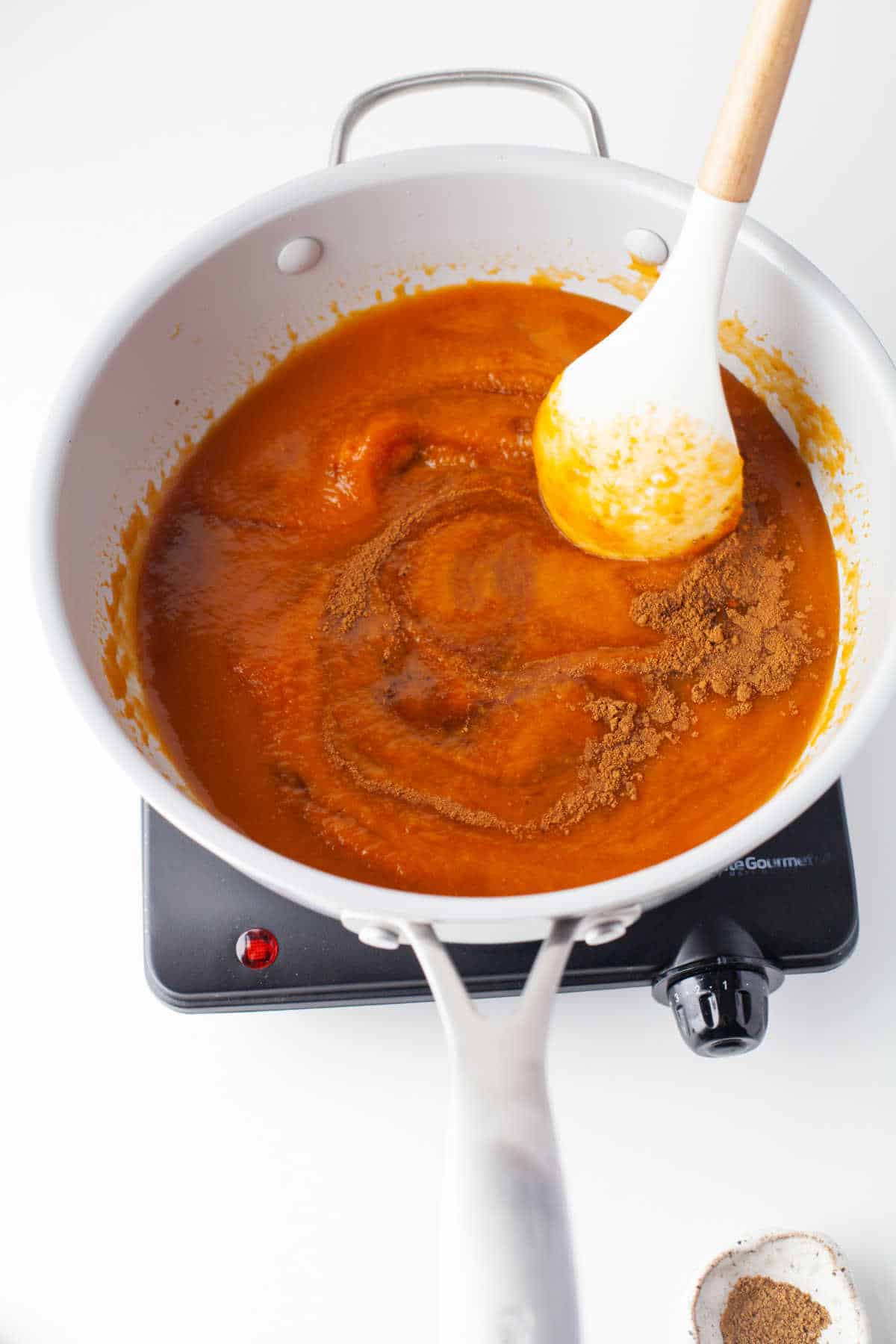 A wooden spoon stirring spices into pumpkin mixture in a skillet. 
