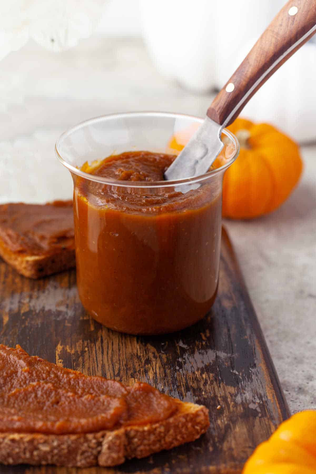 A jar of pumpkin butter sitting on a wooden cutting board. 