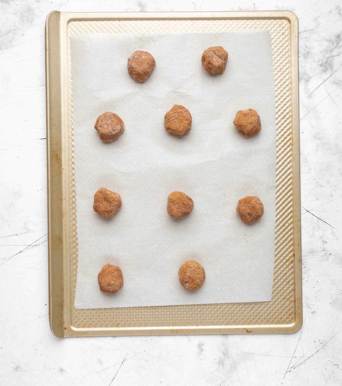 Scoops of pumpkin snickerdoodle cookie dough on a parchment lined baking sheet. 