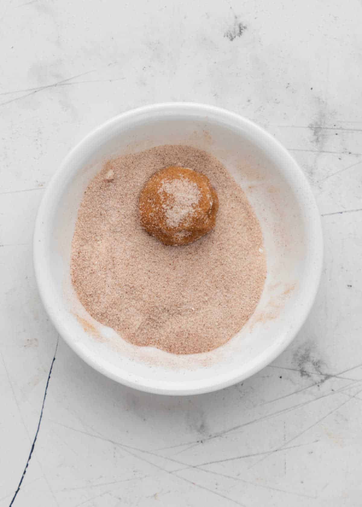 A ball of pumpkin snickerdoodle cookie dough rolling in cinnamon sugar. 