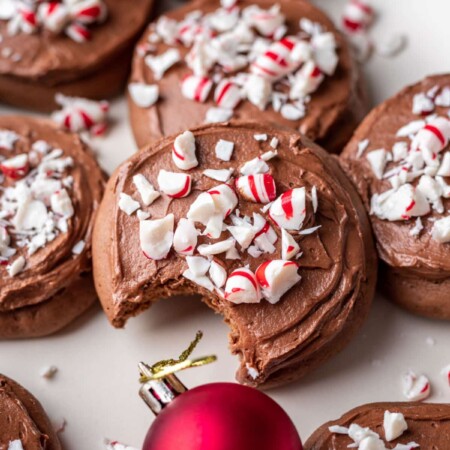 Overlapping stack of frosted chocolate peppermint cookies next to a red ornament.