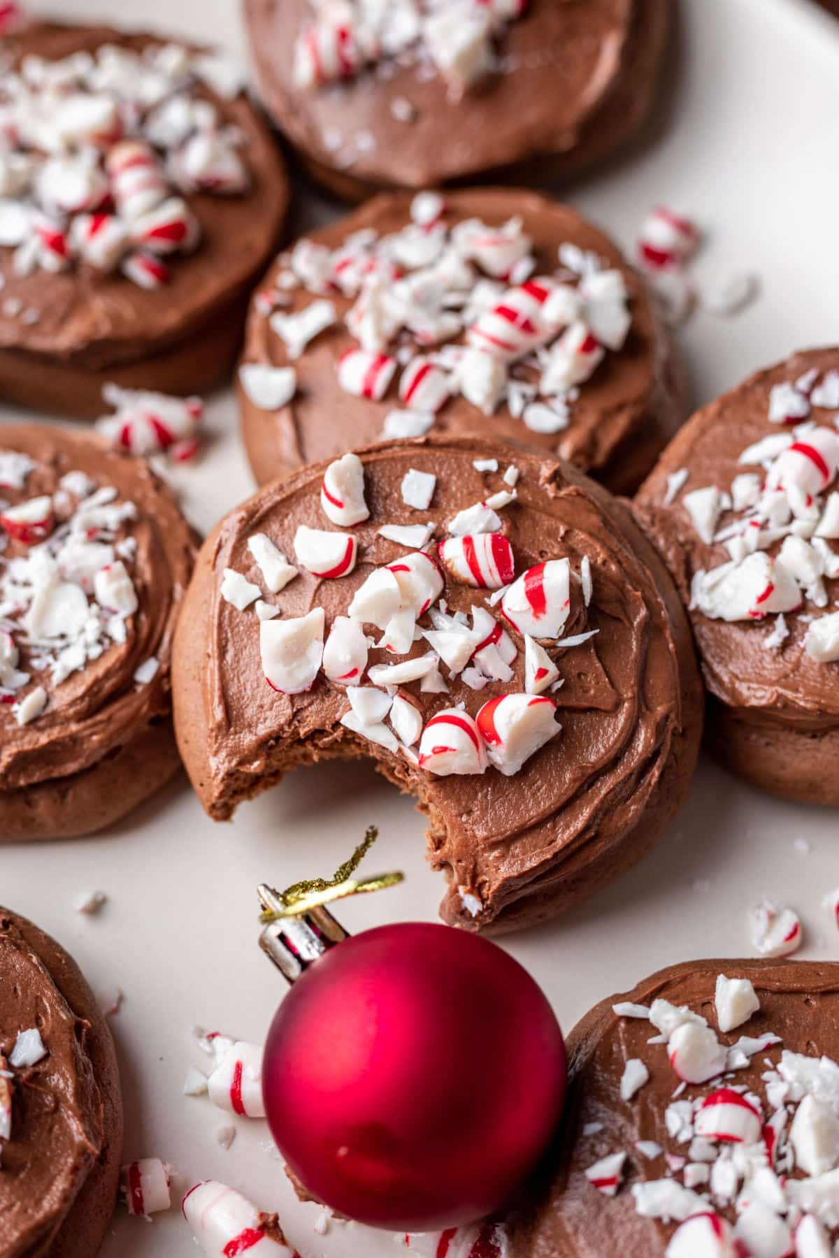 Overlapping stack of frosted chocolate peppermint cookies next to a red ornament.  