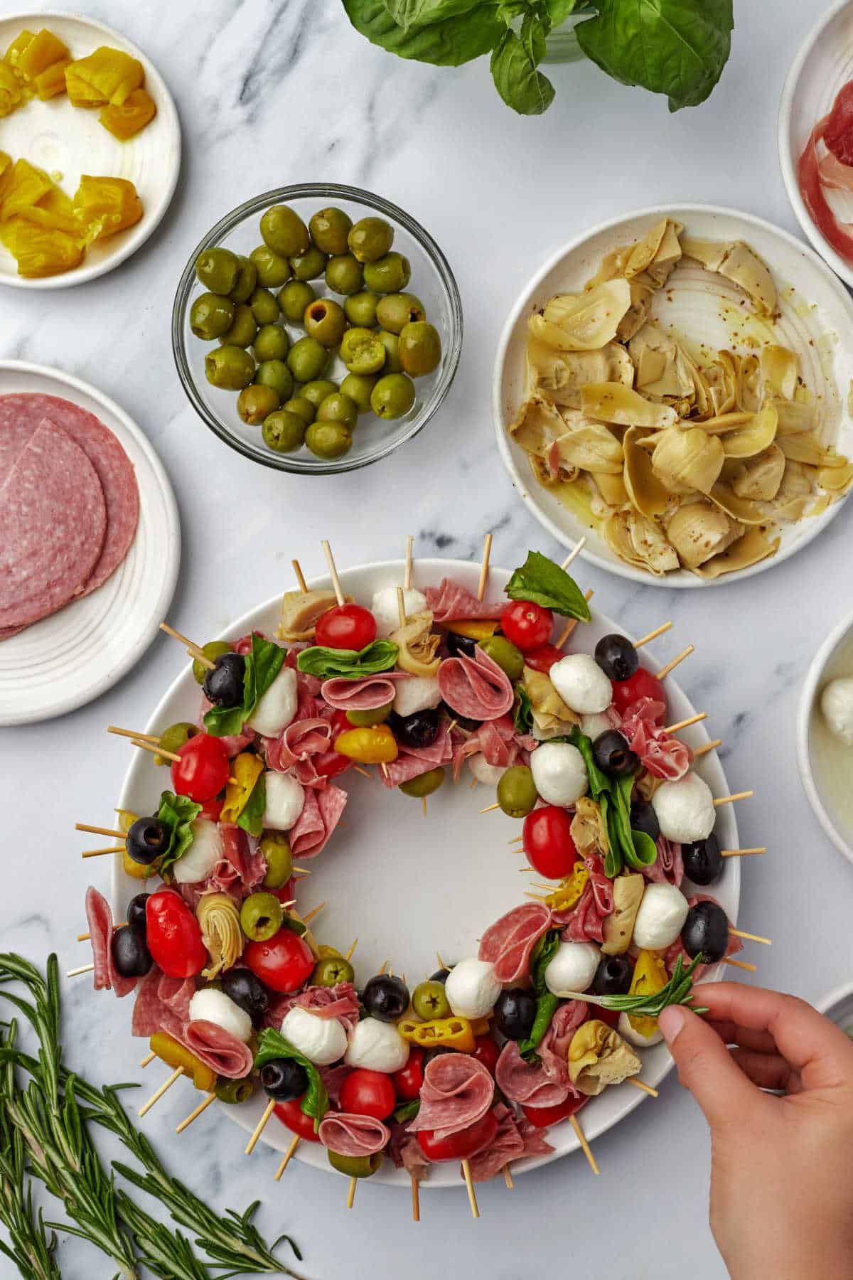 A hand placing rosemary sprigs on a charcuterie wreath.