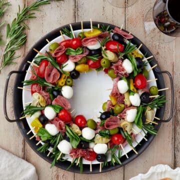 A charcuterie wreath surrounded by glasses of wine and sliced baguette.