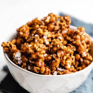 A white bowl filled with caramel corn on a blue linen.