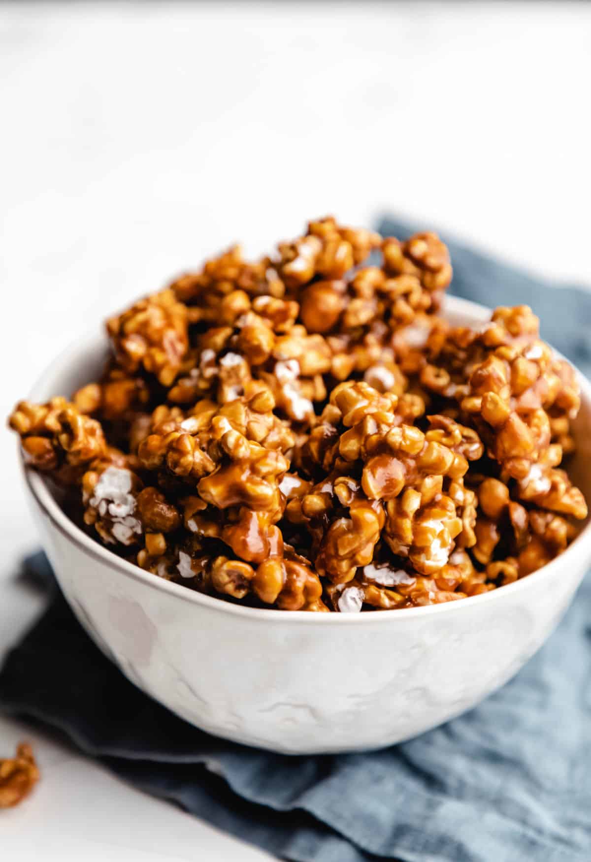 A white bowl filled with caramel corn on a blue linen. 