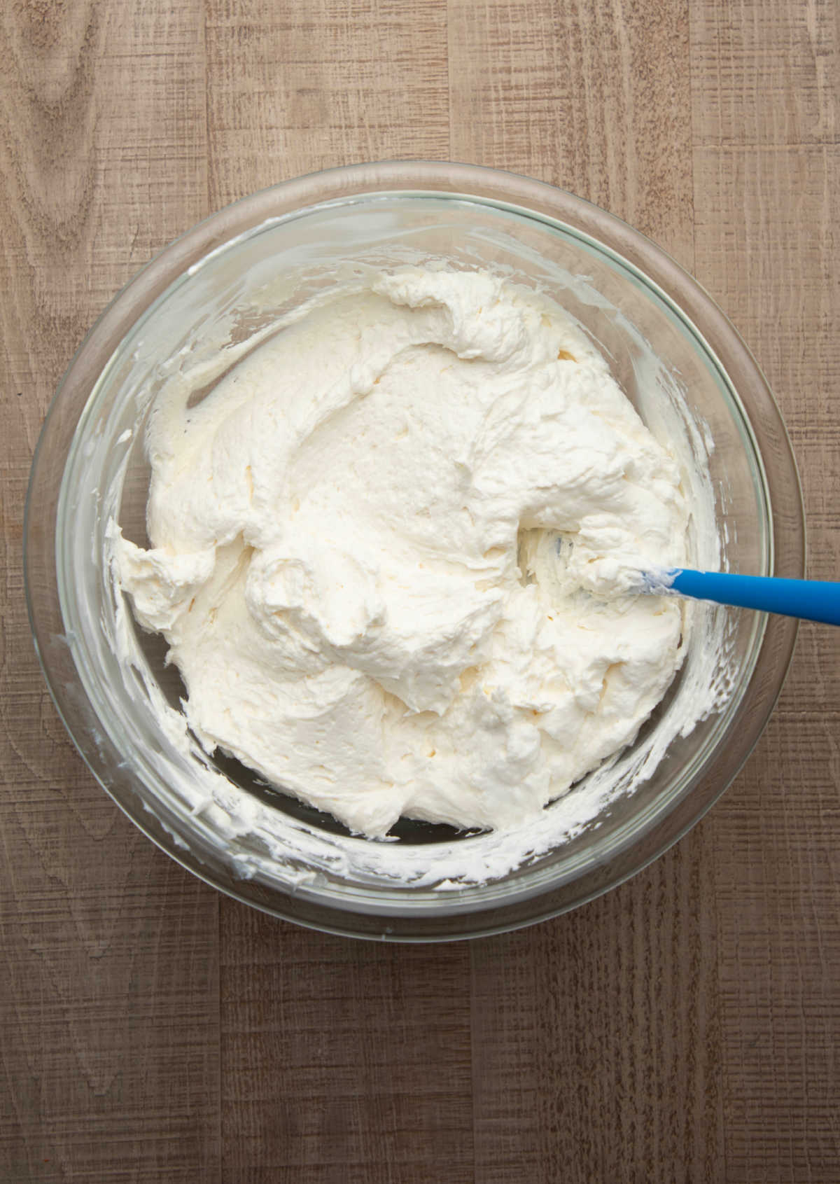 Whipped topping folded into cheesecake mixture in a glass mixing bowl. 