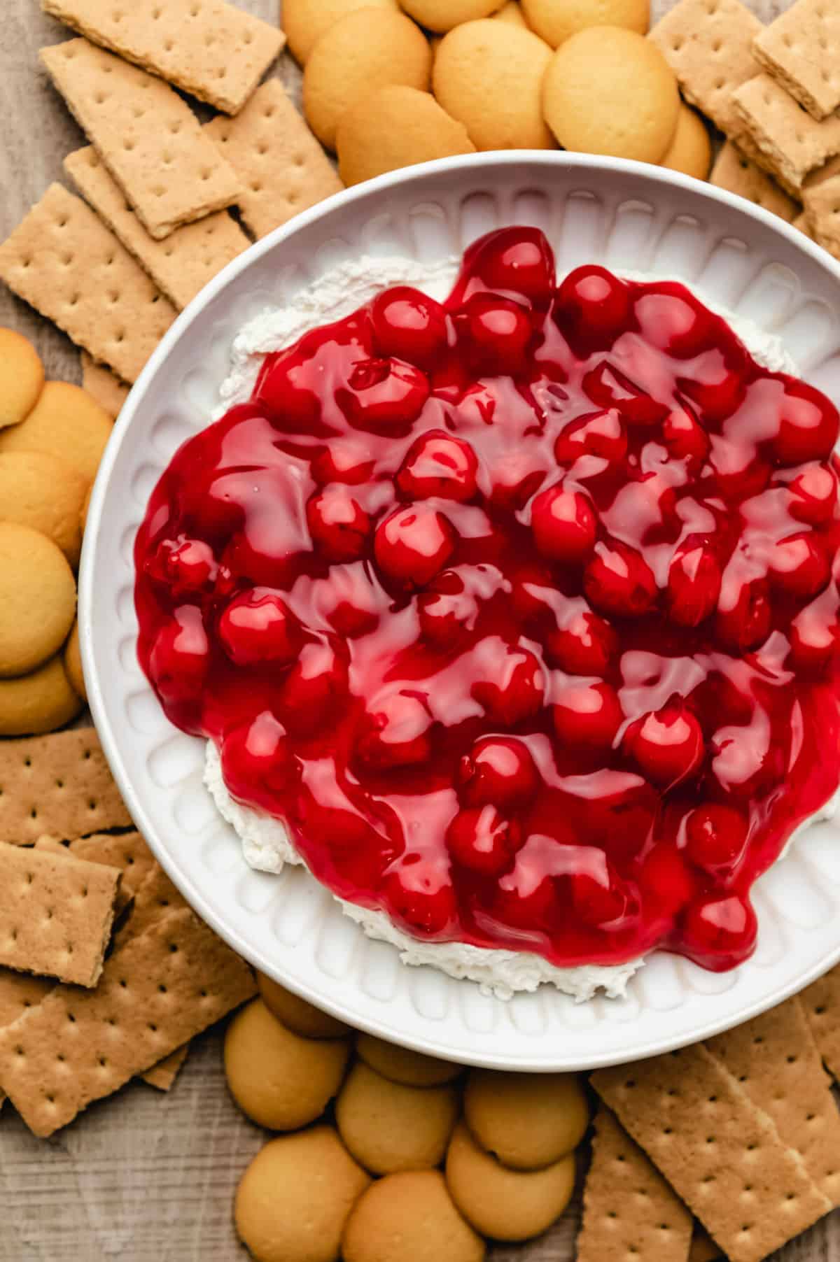 A dish of cherry cheesecake dip surrounded by vanilla wafers and graham cracker pieces.