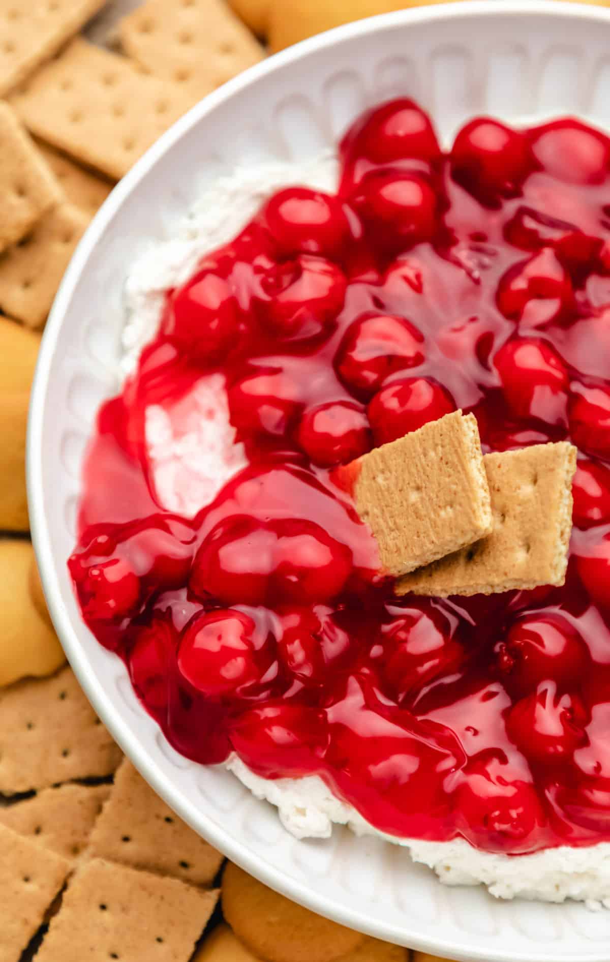 Two graham cracker pieces scooping up cherry cheesecake dip. 