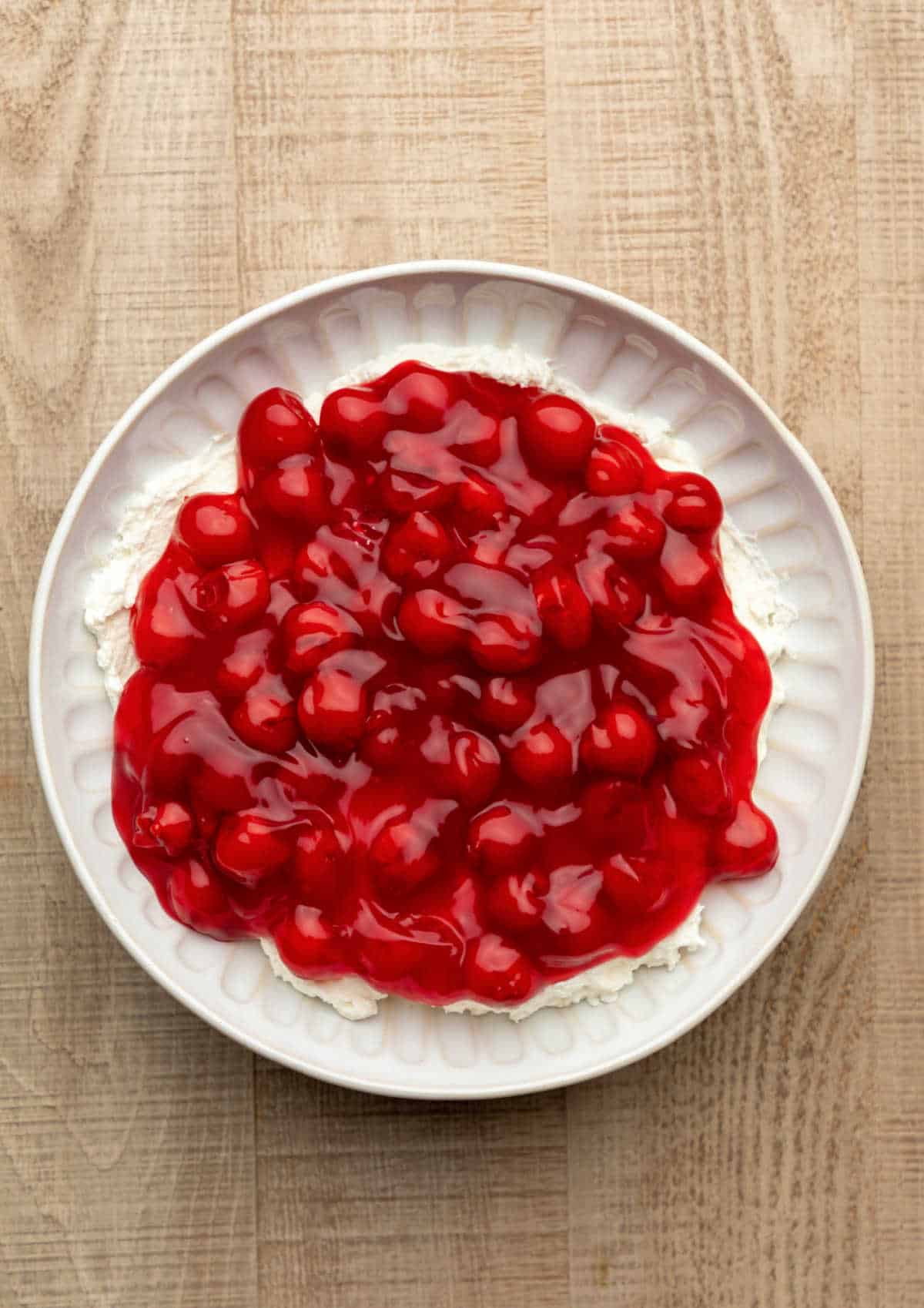Cherry pie filling on top of no bake cheesecake mixture in a dish.