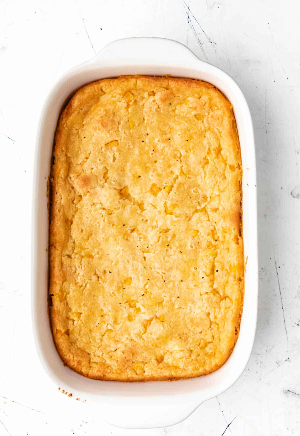 A baked Jiffy corn casserole in a white baking dish. 
