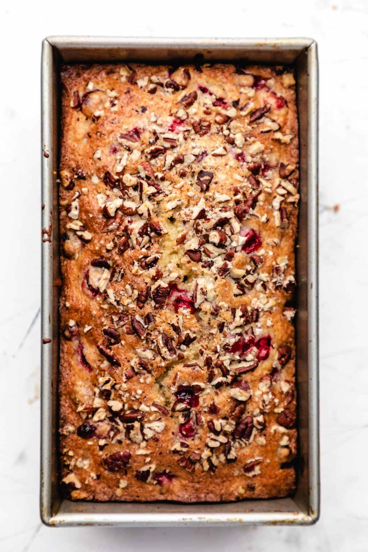 Baked loaf of cranberry nut bread in a loaf pan. 