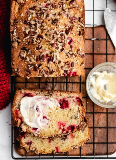 A half buttered slice of cranberry nut bread next to the loaf.