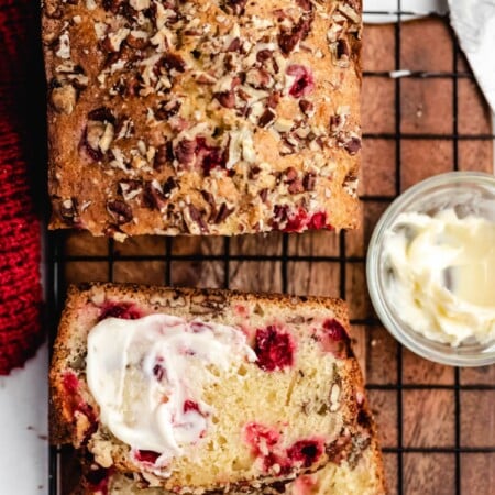 A half buttered slice of cranberry nut bread next to the loaf.