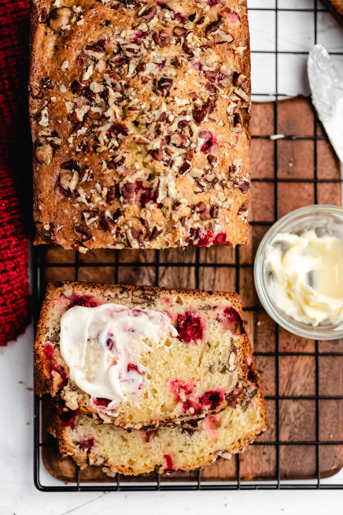 A half buttered slice of cranberry nut bread next to the loaf. 