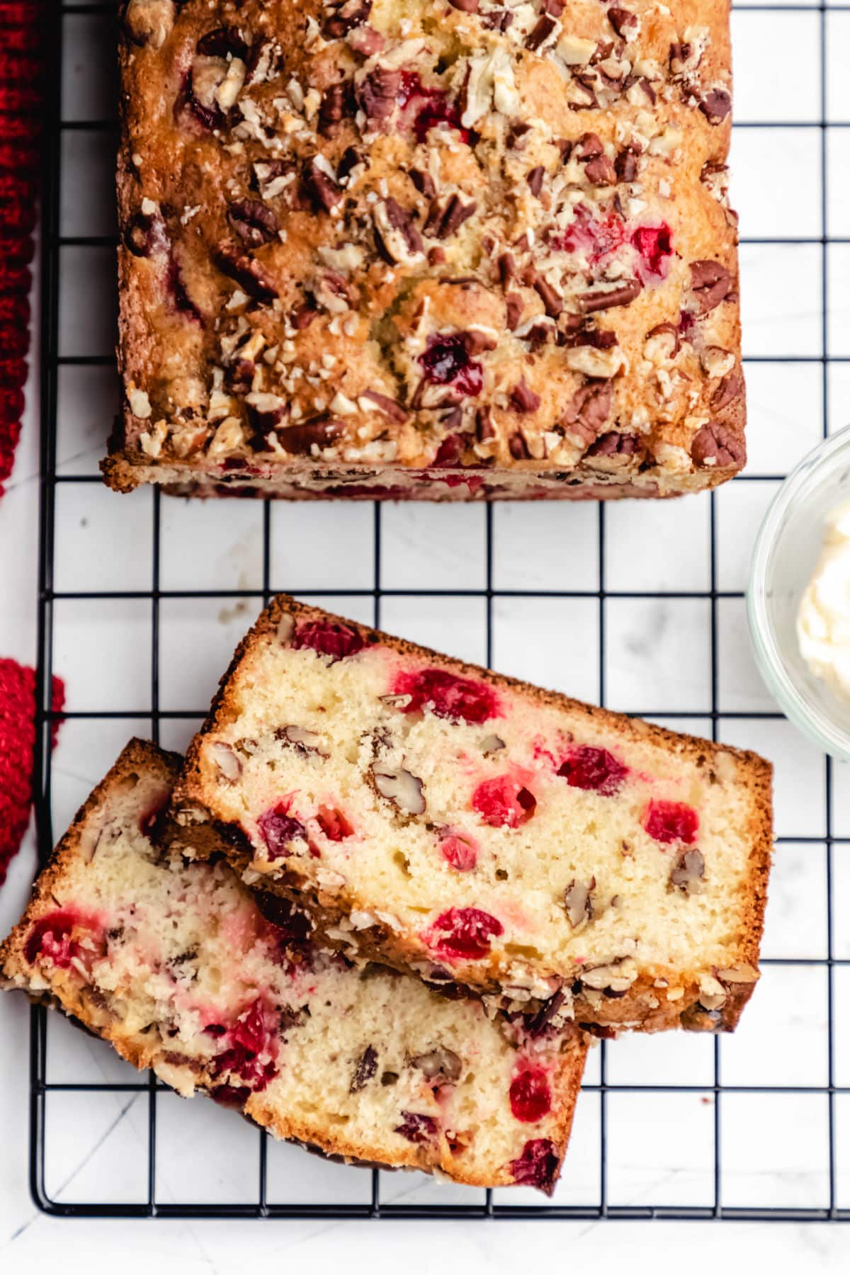 Two slices of cranberry nut bread on a cooling rack next to the loaf. 