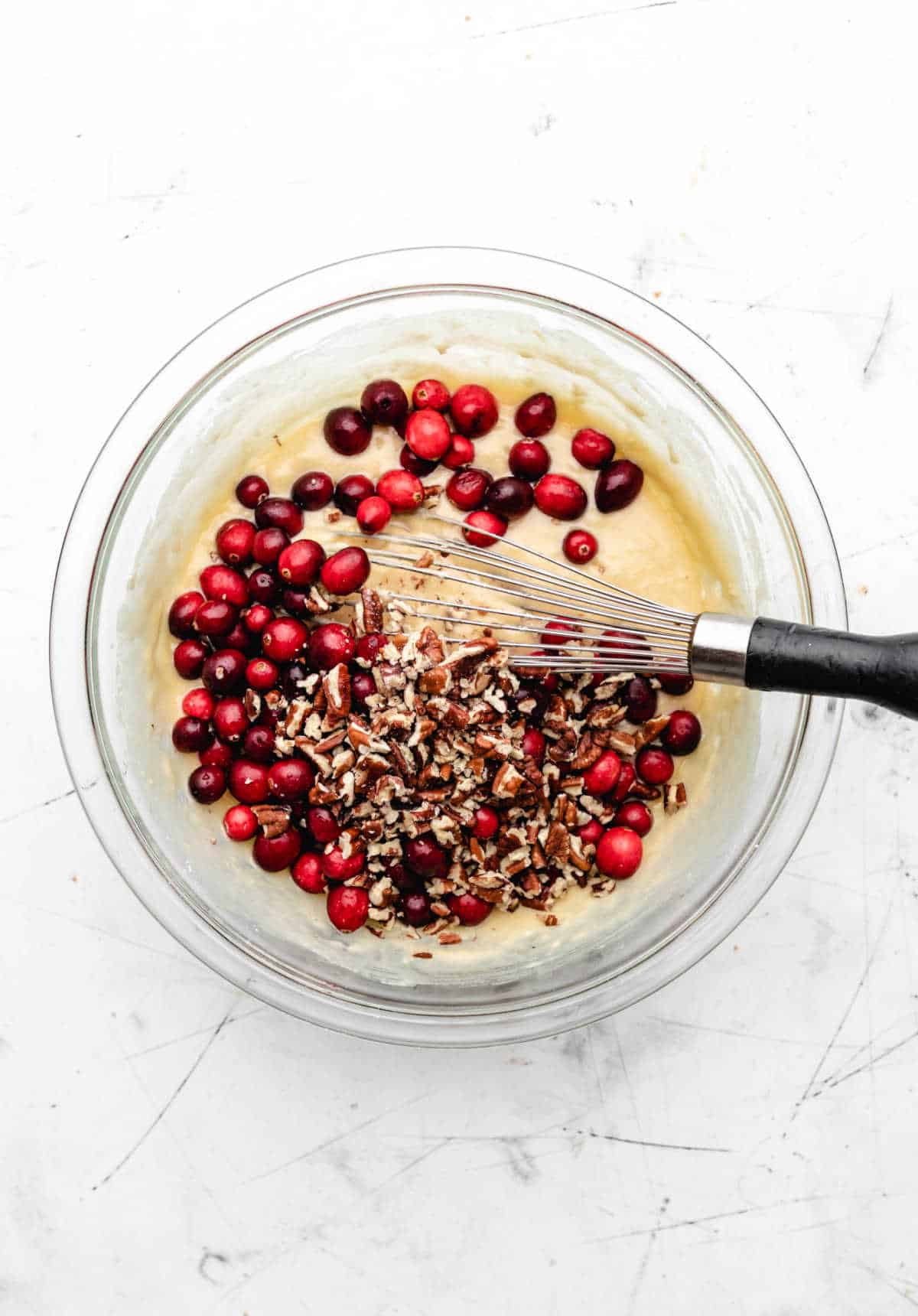 Fresh cranberries and chopped pecans on cranberry nut bread batter. 